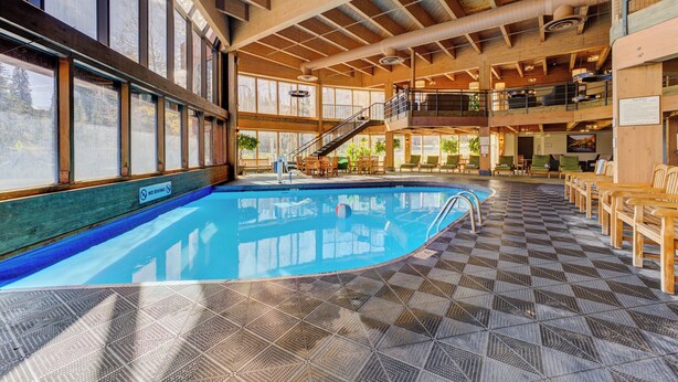 An indoor swimming pool with a no diving sign, wooden deck, and a staircase leading to an upper level.