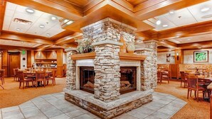 A spacious lobby with a stone fireplace, wooden ceiling beams, and a tiled floor.