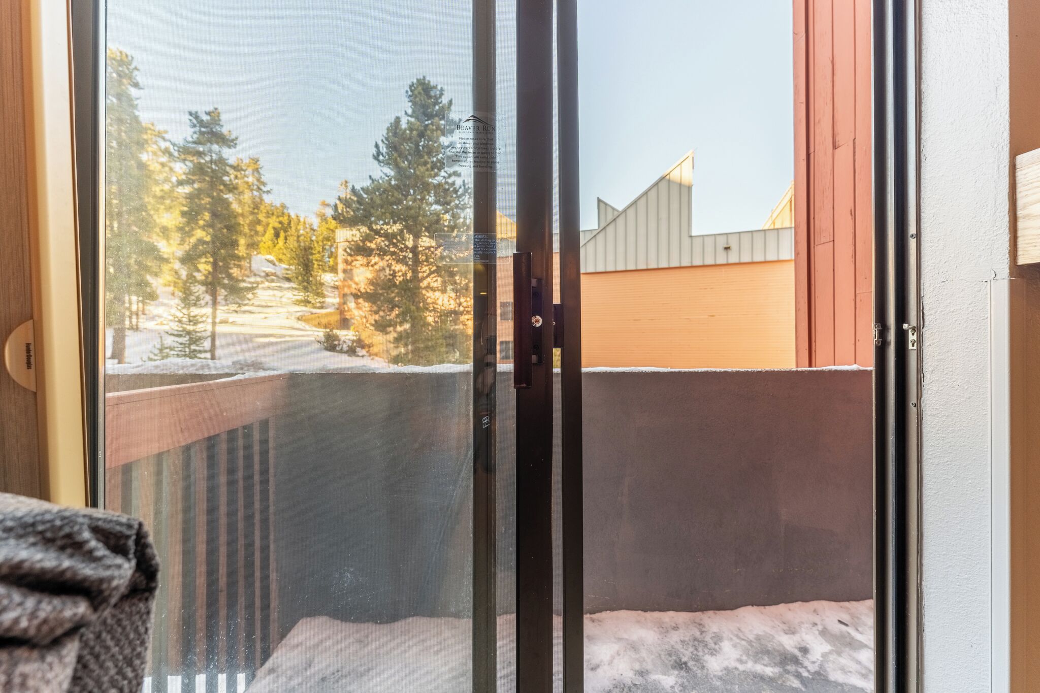 Vue depuis un balcon doté d’une rambarde en métal, donnant sur un paysage enneigé avec des arbres et un bâtiment en arrière-plan.