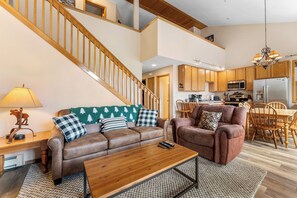 A spacious living room with a brown leather sofa, a wooden coffee table, and a staircase leading to an upper level.