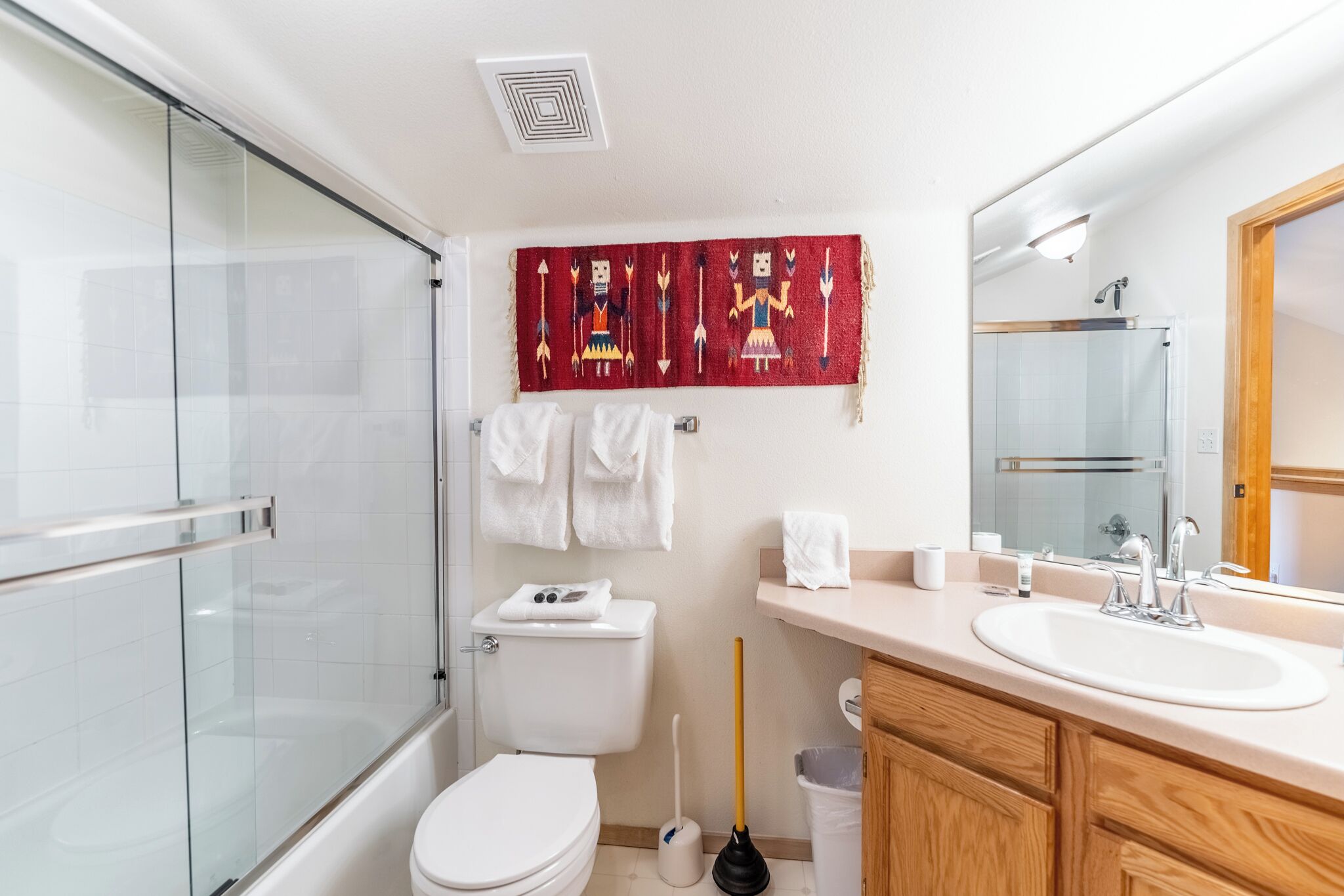 A modern bathroom with a glass shower enclosure, a white toilet, a red decorative towel, a sink with a mirror, and wooden cabinets.