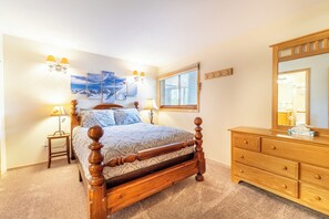 A bedroom with a wooden bed, bedside lamps, a dresser, a mirror, and artwork on the wall.