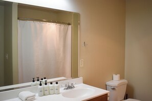 A bathroom with a white sink, mirror, and toilet. There are toiletries on the sink and a shower curtain visible in the mirror. - Spacious Studio Retreat I Century (Orem)