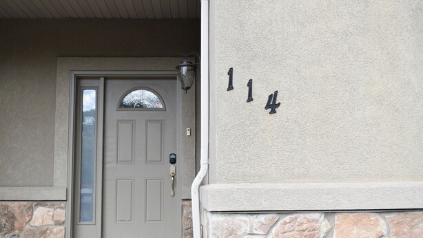 Husnummer 114 på en struktureret væg, en grå dør med glasrude og en stensokkel.