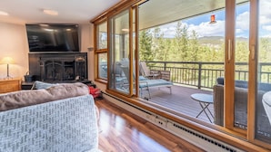 A cozy living room with a fireplace, a large TV, and a balcony with outdoor furniture. - P2070-3 (Keystone)