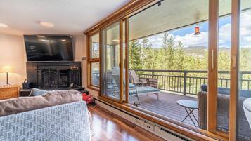 A cozy living room with a fireplace, a large TV, and a balcony with outdoor furniture.
