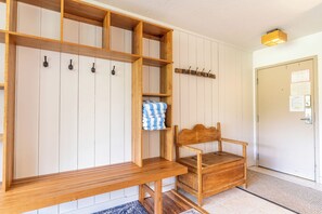 A wooden bench and chair in a hallway with a coat rack and a door with a bulletin board.