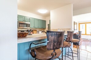 A kitchen with teal cabinets, a wooden bowl, and bar stools.