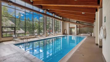 An indoor swimming pool with clear views of the outdoors, large windows, and wooden ceiling beams.