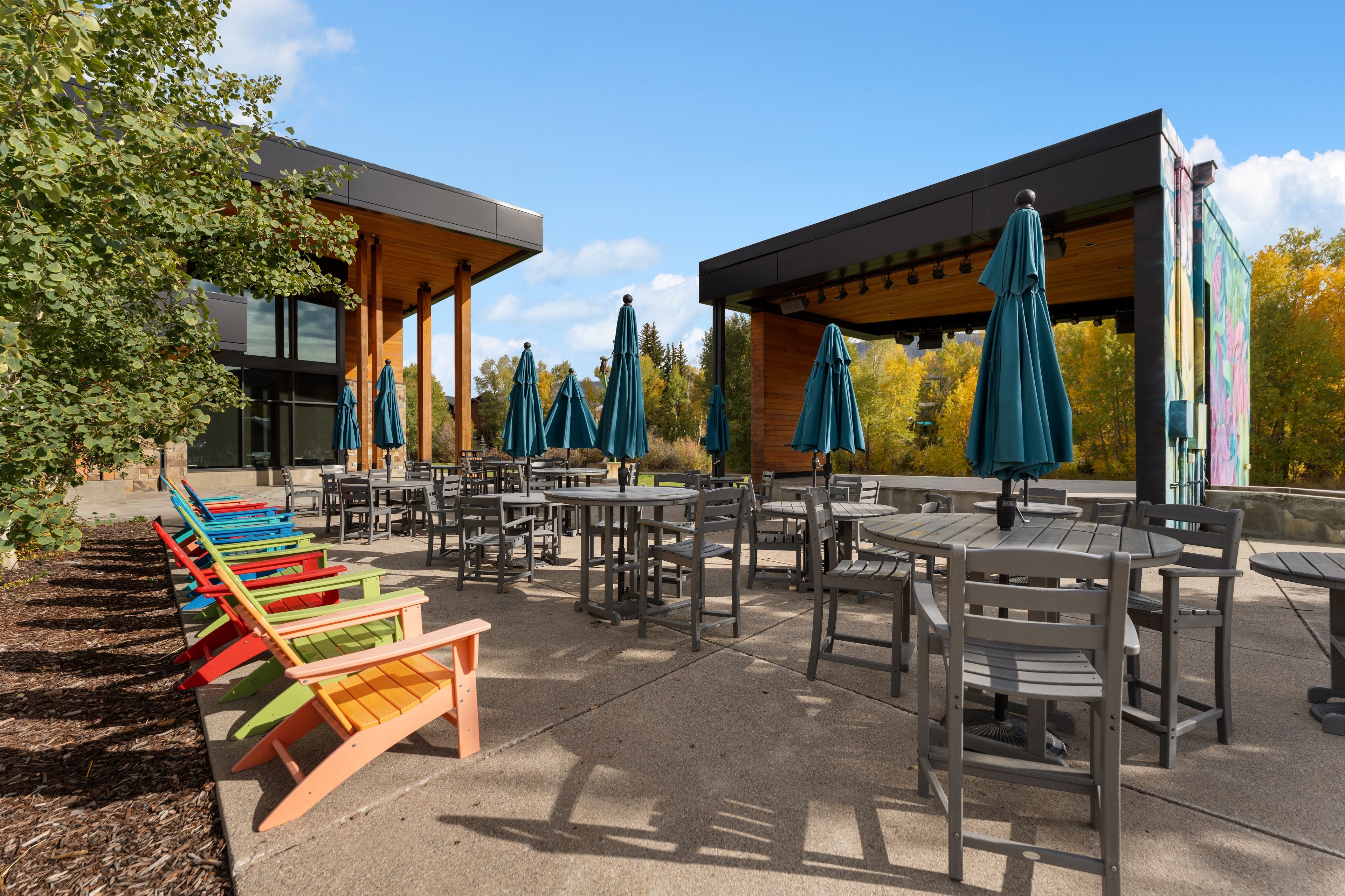 An outdoor seating area with tables and chairs, surrounded by trees and a building with a modern design.