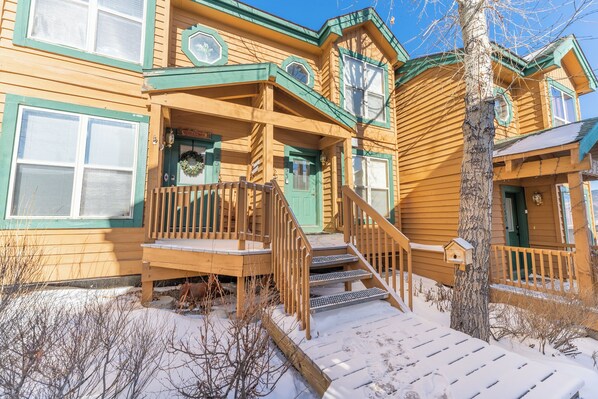 A wooden house with a porch, steps, and a snow-covered ground.