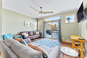 A living room with a brown leather sofa, a grey couch, a blue patterned rug, a ceiling fan, and a TV mounted on the wall. - Srt253-3 (Silverthorne)