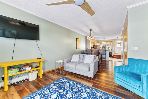 A living room with a grey sofa, a blue armchair, a yellow TV stand, and a patterned rug.