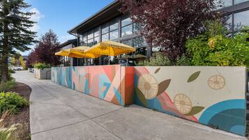 A colorful wall with abstract patterns, a building with large windows, and yellow umbrellas.