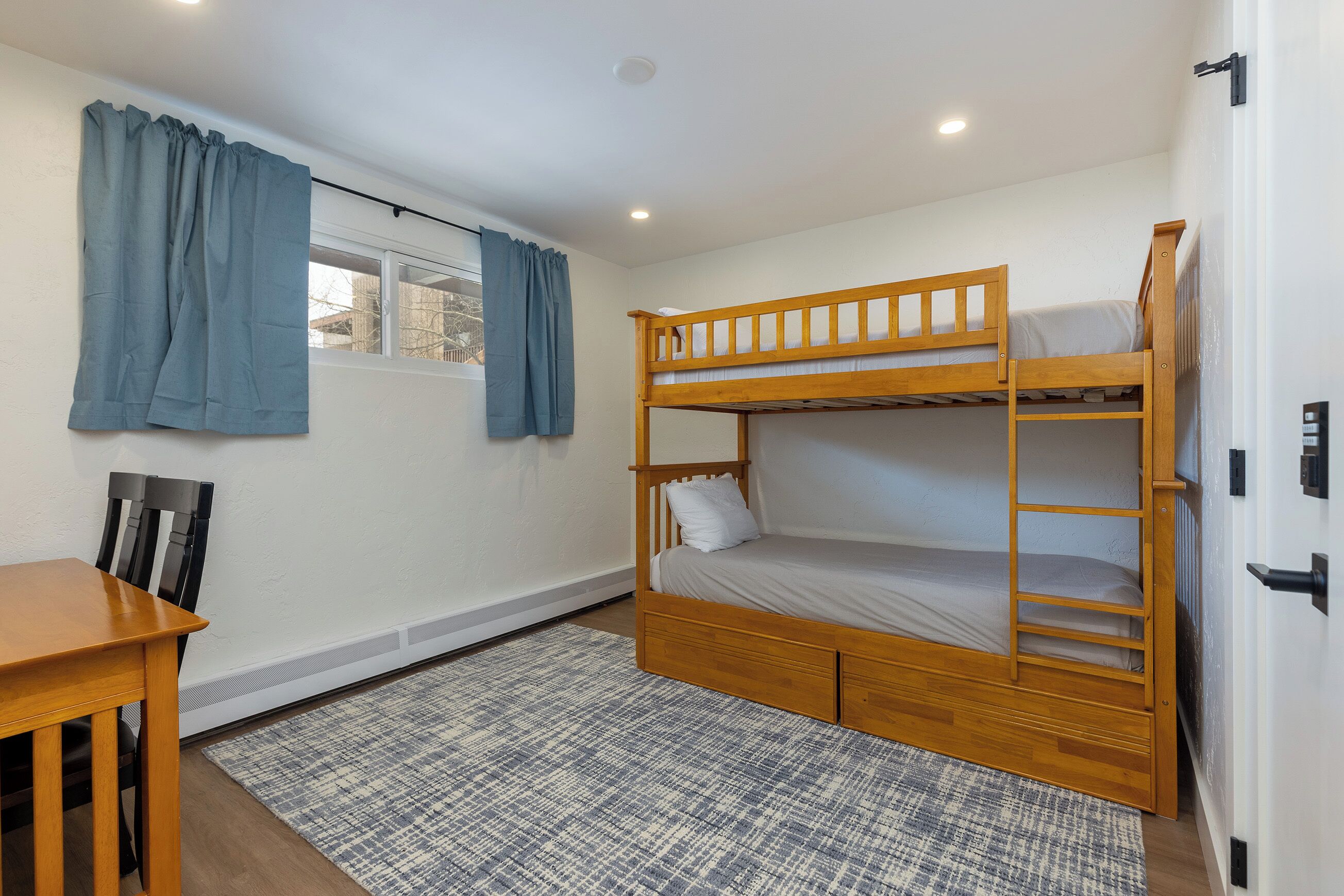 A bunk bed room with a window, a desk, and a chair.