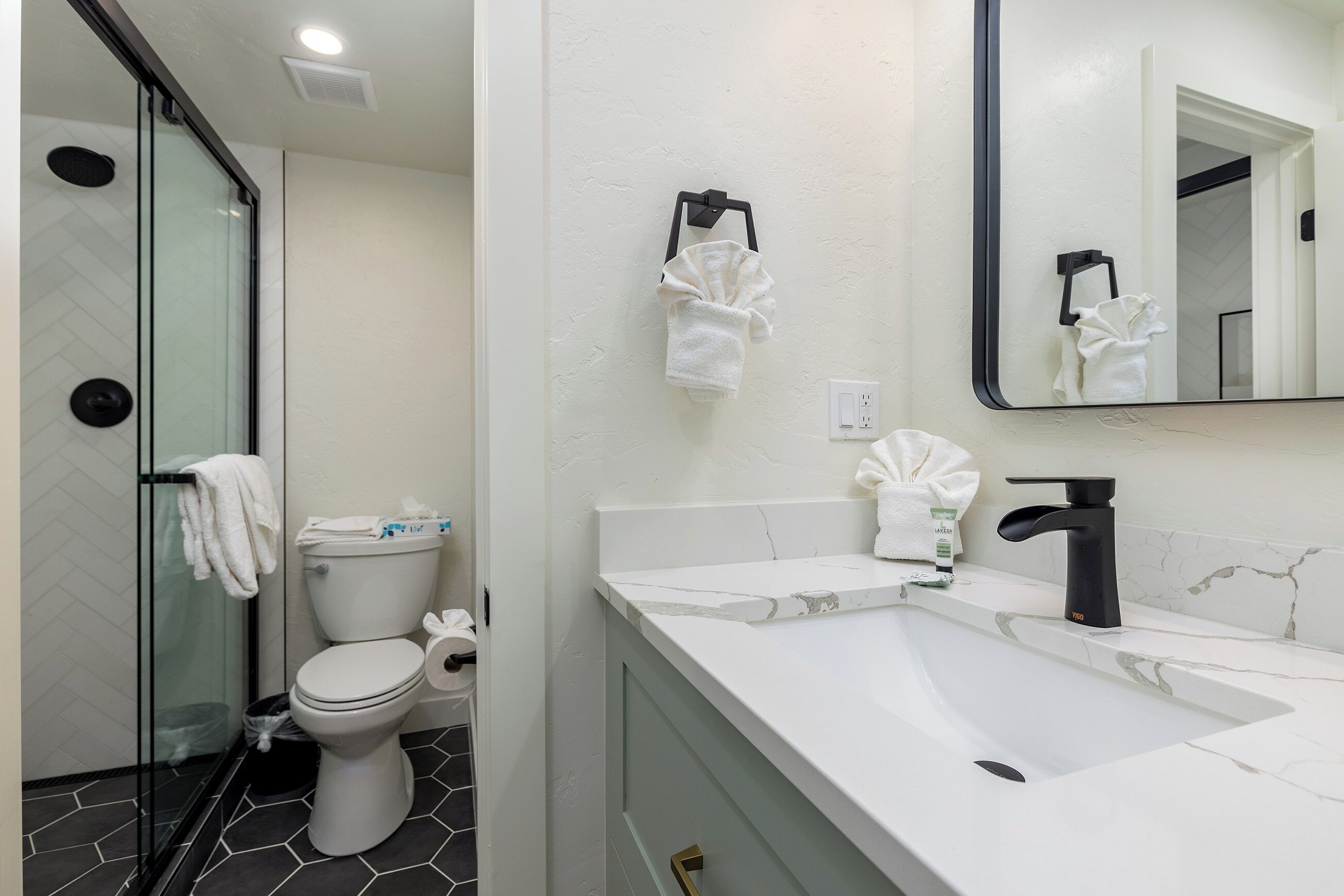 A modern bathroom with a glass shower enclosure, a white toilet, a sink with a black faucet, and a mirror above the sink.