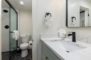 Een moderne badkamer met een douchecabine van glas, een wit toilet, een wastafel met een zwarte kraan en een spiegel boven de wastafel.