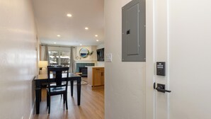 Une chambre d’hôtel moderne avec un plancher en bois, un coin repas comprenant une table et des chaises, une cuisine avec des meubles en bois et une porte grise dotée d’un système de verrouillage à clavier.