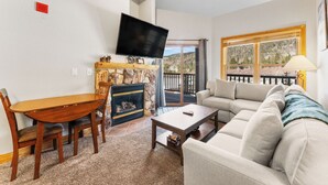 A living room with a fireplace, a television mounted on the wall, a sofa, and a dining table with chairs. - Hr5982-2 (Keystone)