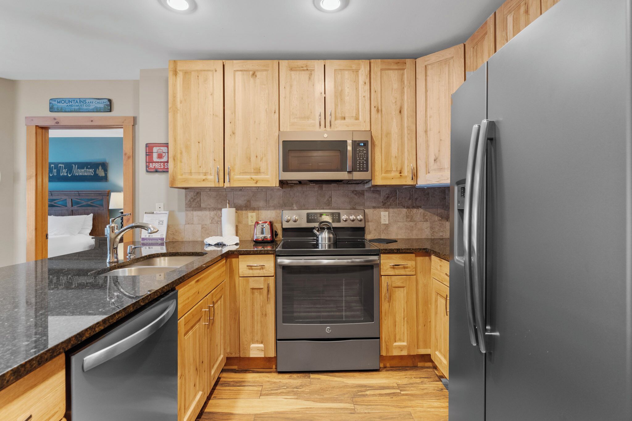 A kitchen with wooden cabinets, a stainless steel refrigerator, a microwave, a stove, and a dishwasher.