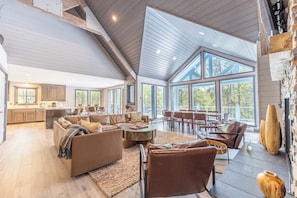 A spacious living area with a high ceiling, large windows, and a modern kitchen.