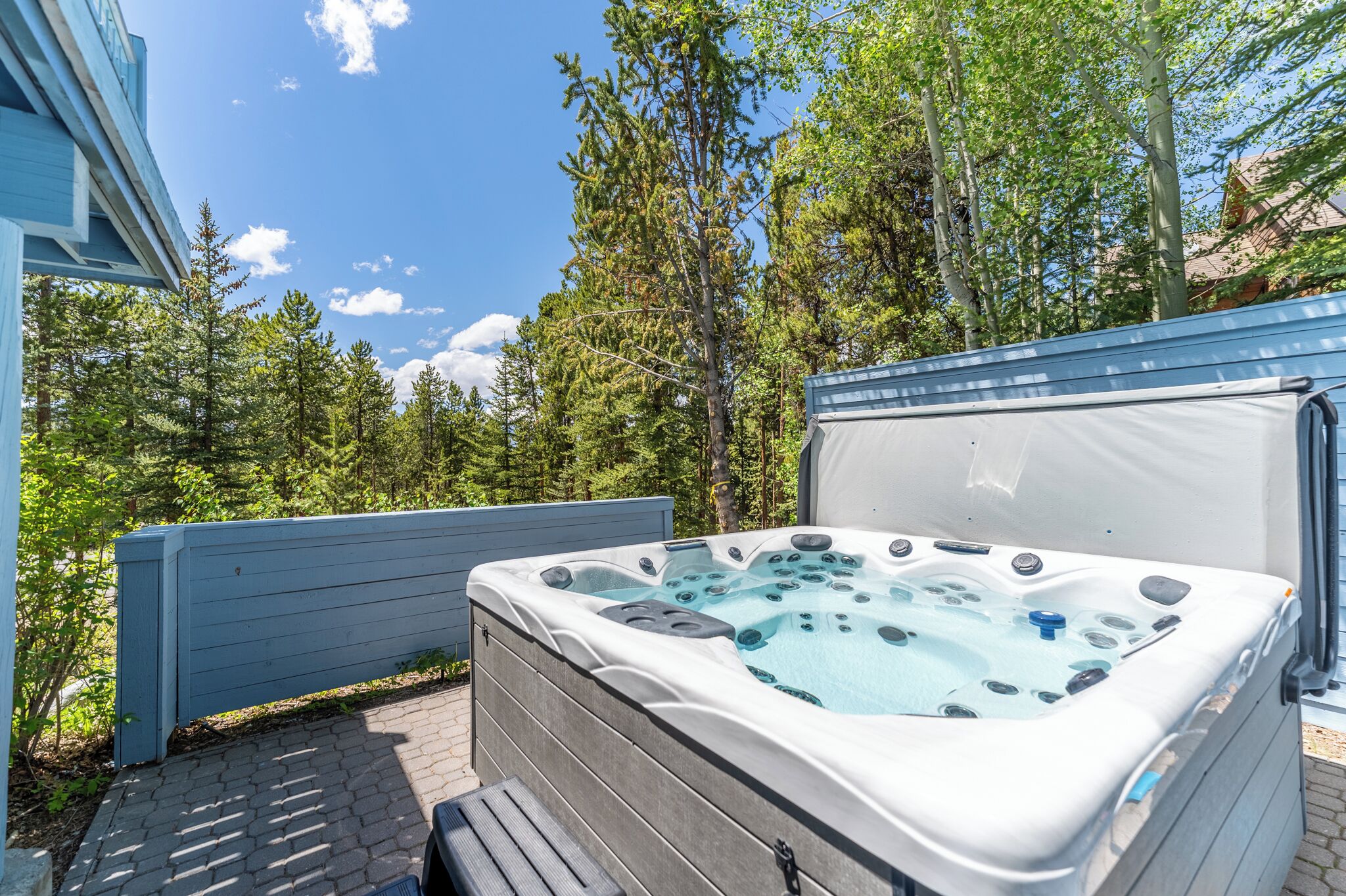 Een hottub in een achtertuin met een houten terras, omgeven door bomen en een huis.