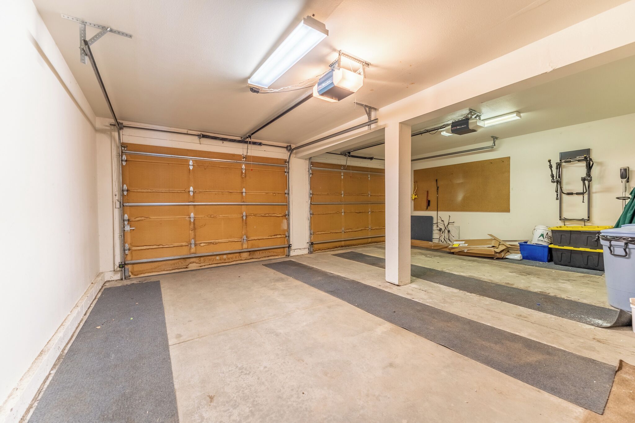 A garage with two wooden garage doors, a concrete floor, and a ceiling with fluorescent lighting.