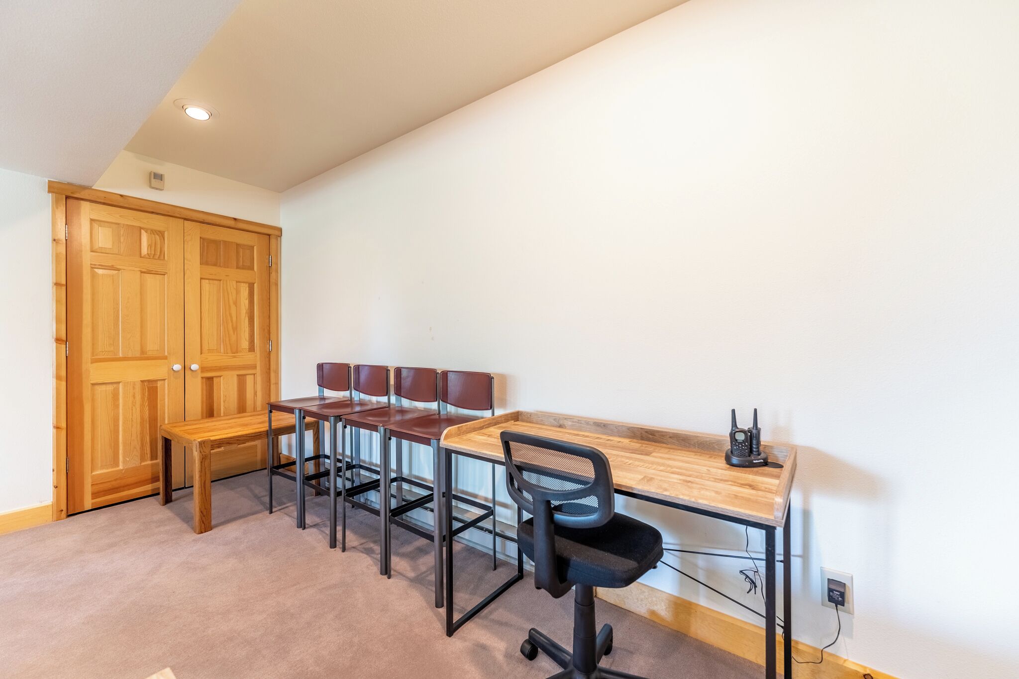 A room with a wooden desk, four chairs, a bench, and a wooden wardrobe.