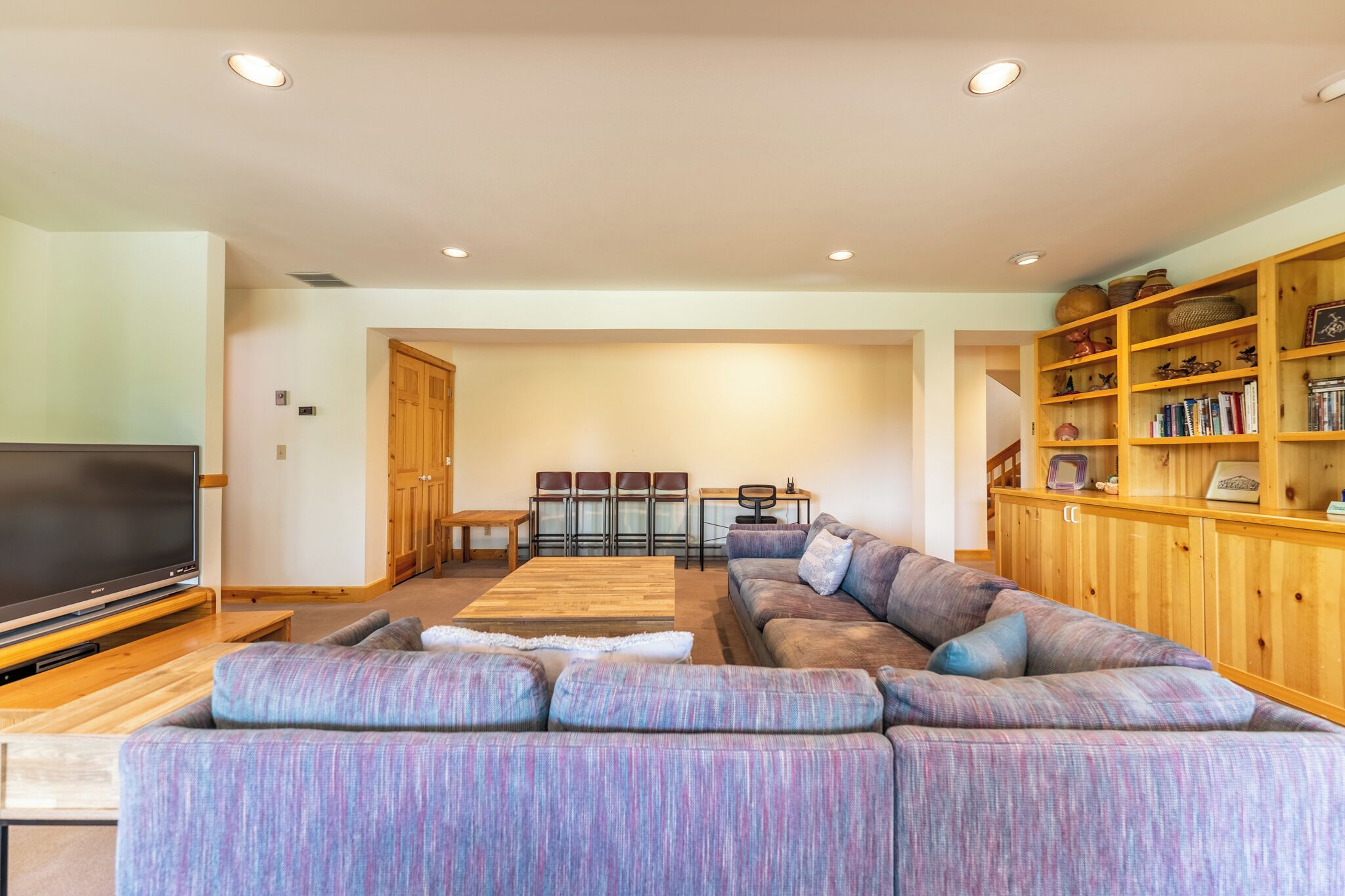 Een moderne woonkamer met een grote flatscreen-tv, een hoekbank, een houten salontafel en een boekenkast vol boeken en decoratieve objecten.
