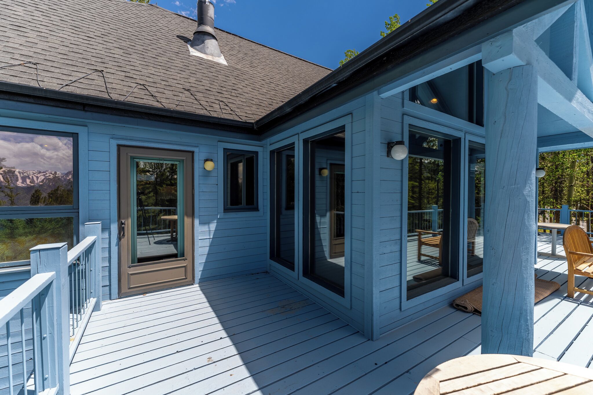A blue wooden deck with glass doors and windows, outdoor furniture, and a view of mountains.