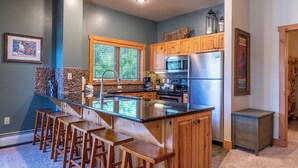Una cocina con una isla central, taburetes de madera, estufa integrada y un refrigerador.