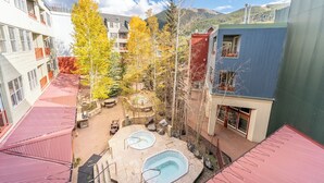 A courtyard with two hot tubs, surrounded by buildings with balconies and a mountain backdrop. - Sm8203-1 (Keystone)