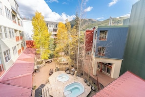 Un patio con dos jacuzzis, rodeado de edificios con balcones y un telón de fondo de montañas.