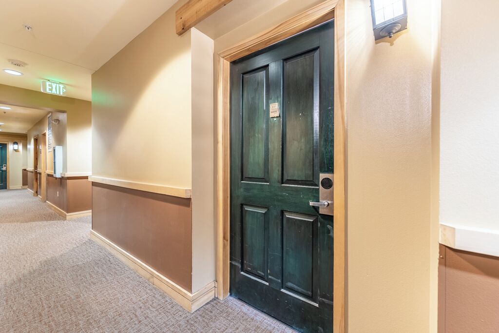 A hotel hallway with a green door, beige walls, and carpeted flooring.