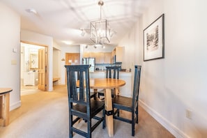 A dining area with a round wooden table and four chairs, a modern chandelier, and a framed picture on the wall.