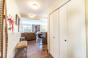 Ein Flur mit einer Bank, einer weißen Tür und Blick in einen Wohnbereich mit einer Couch und einem Esstisch.