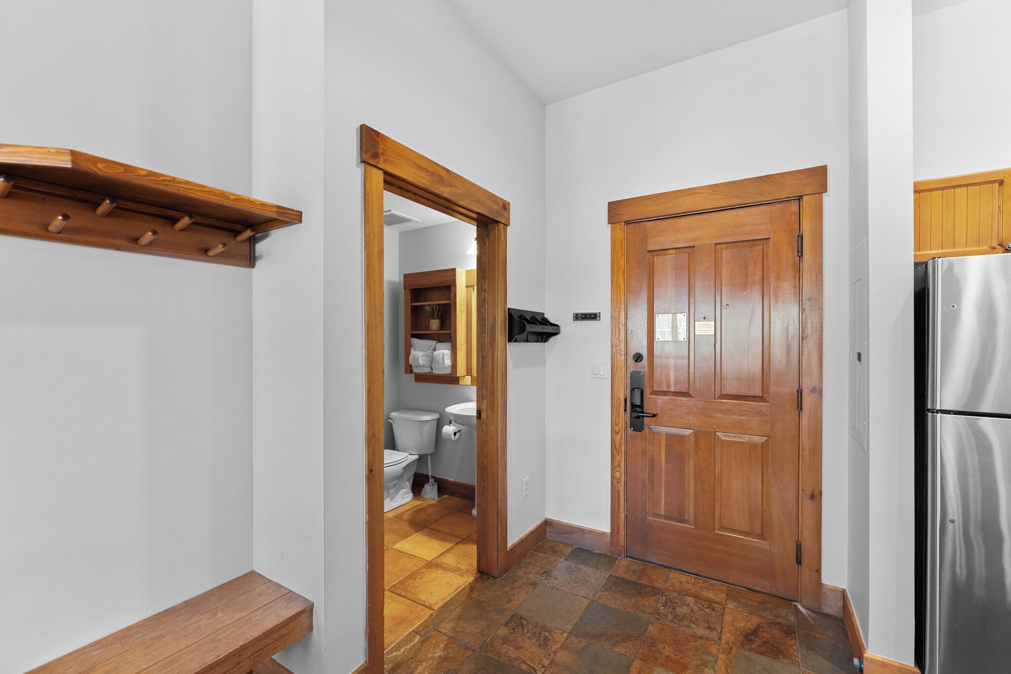 A hallway with a wooden door, a bench, and a refrigerator.