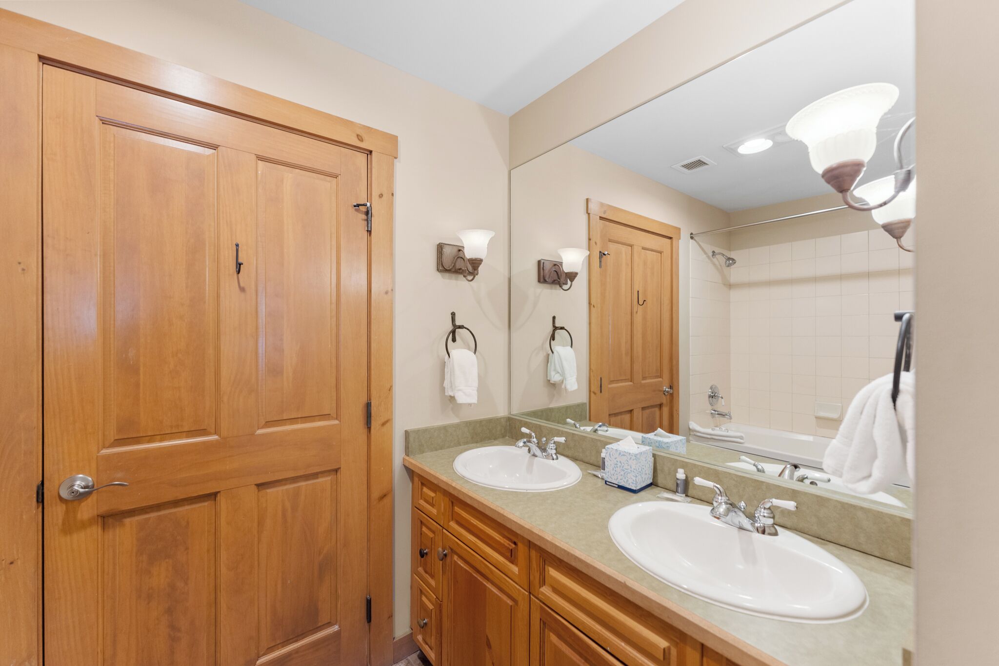 A bathroom with wooden doors, two sinks, a mirror, and a towel rack.