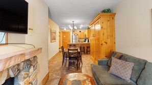 A modern kitchen with wooden cabinets, a dining area with chairs, and a stone fireplace. - Expedition Station #8576 (Keystone)