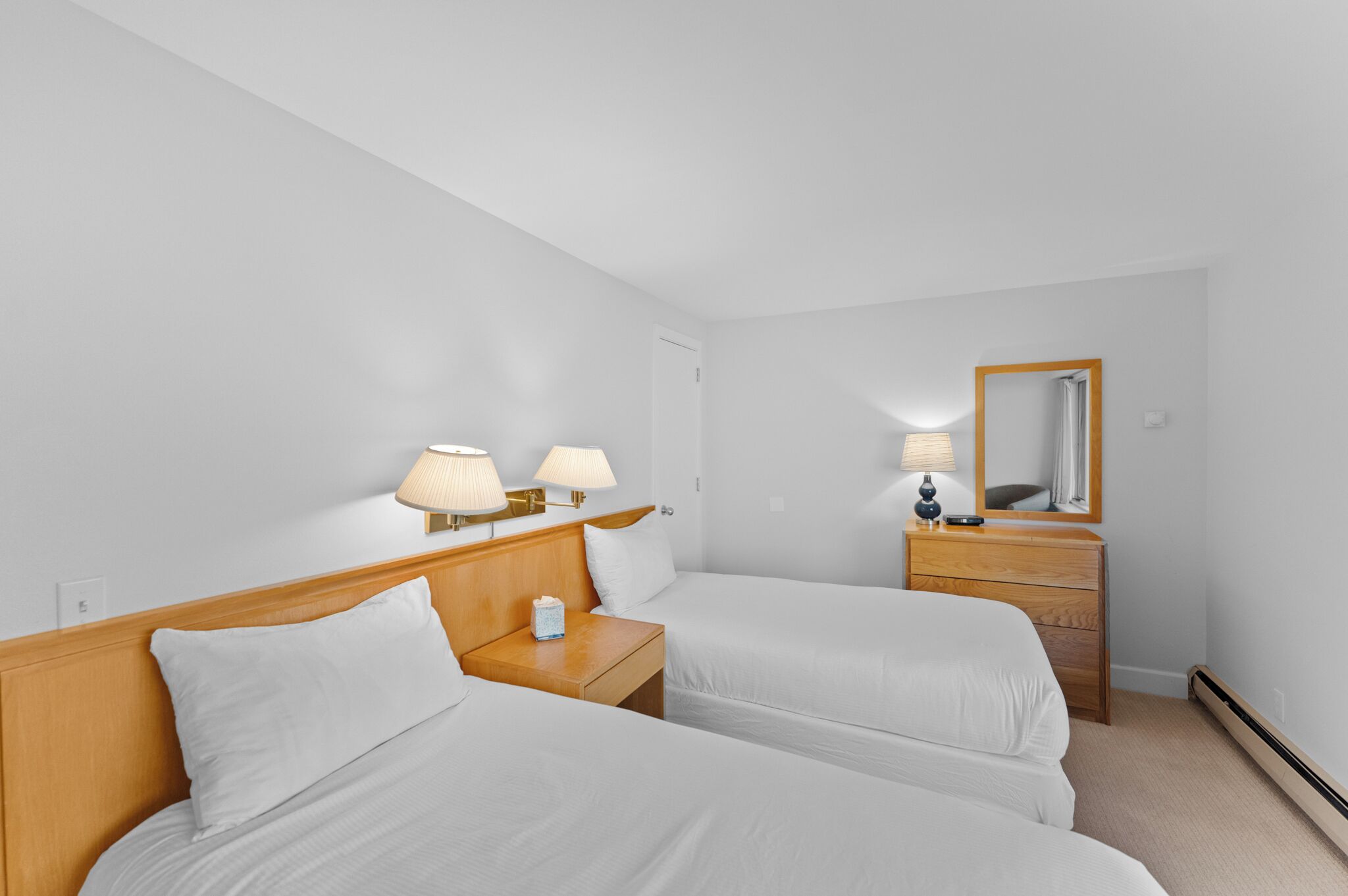 Habitación de hotel con dos camas individuales, una mesita de noche de madera con lámparas, un aparador y un espejo.