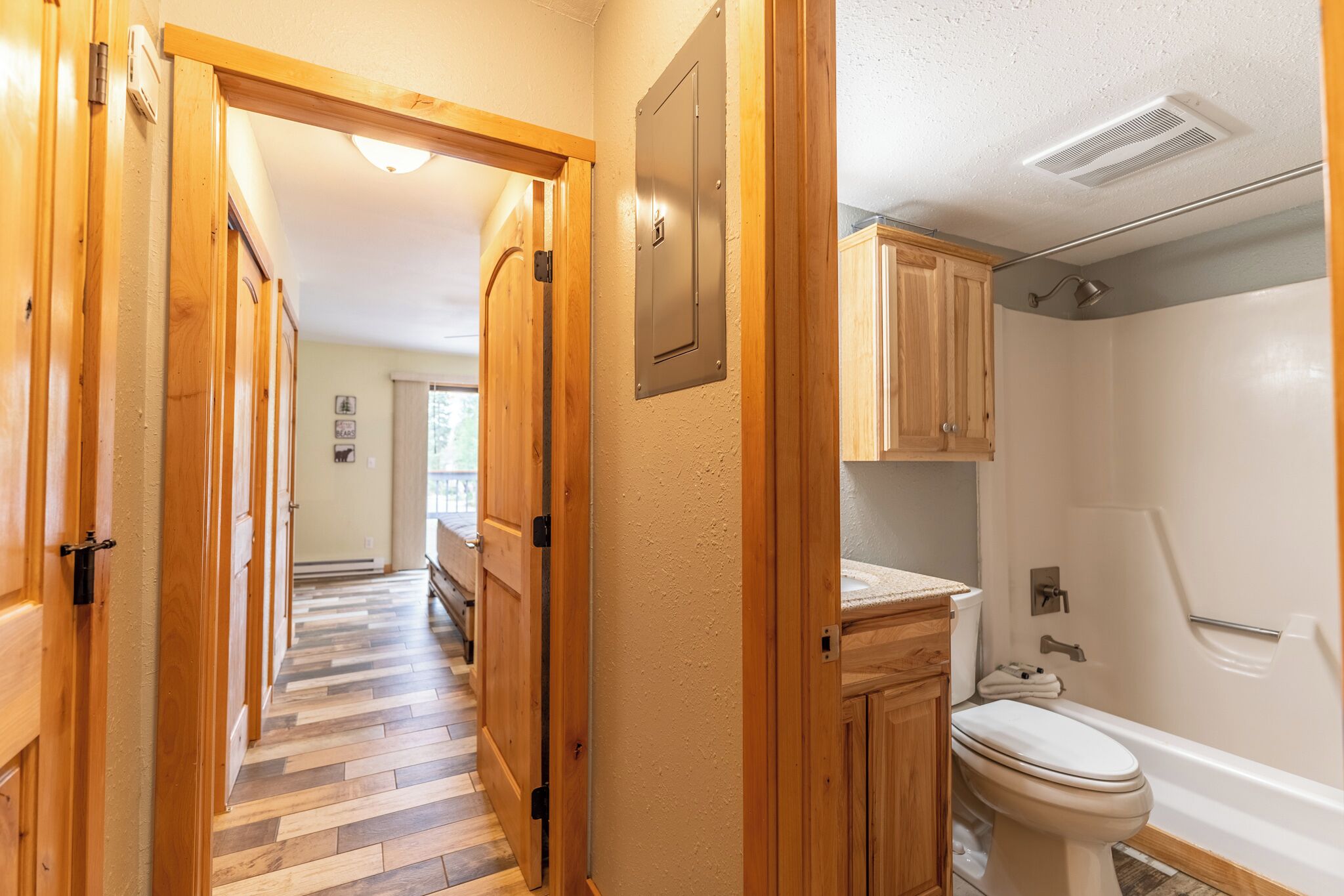 A hallway with wooden doors leading to a bathroom with a toilet, bathtub, and wooden cabinets.
