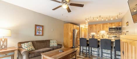 A modern kitchen with wooden cabinets, a stainless steel refrigerator, and a bar area with bar stools.
