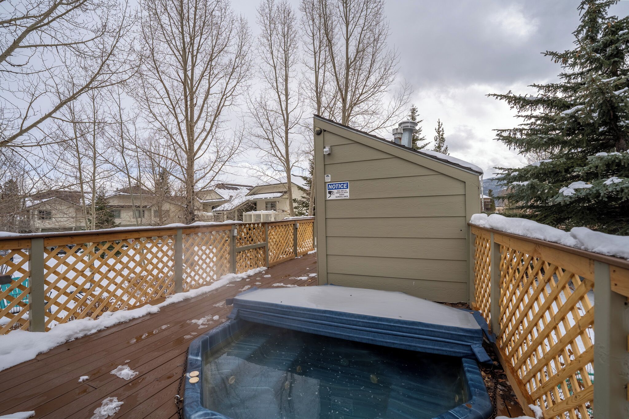 A wooden deck with a hot tub, a wooden fence, and a shed with a 'NOTICE' sign.