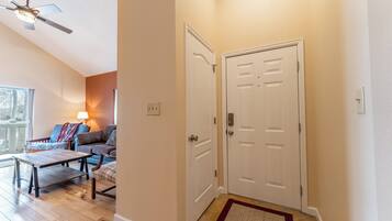 A hallway with a white door, a ceiling fan, a wooden table, and a sofa with a colorful blanket.