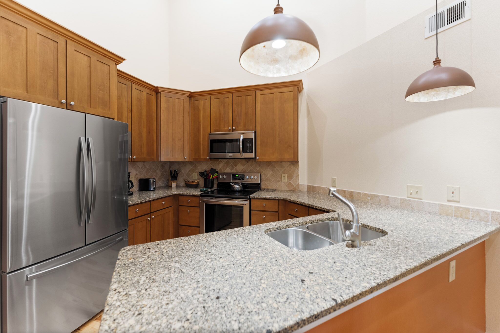 Una cocina con encimeras de granito, electrodomésticos de acero inoxidable, gabinetes de madera e iluminación colgante.