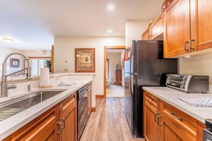 A modern kitchen with wooden cabinets, a stainless steel sink, a black refrigerator, and a built-in oven.
