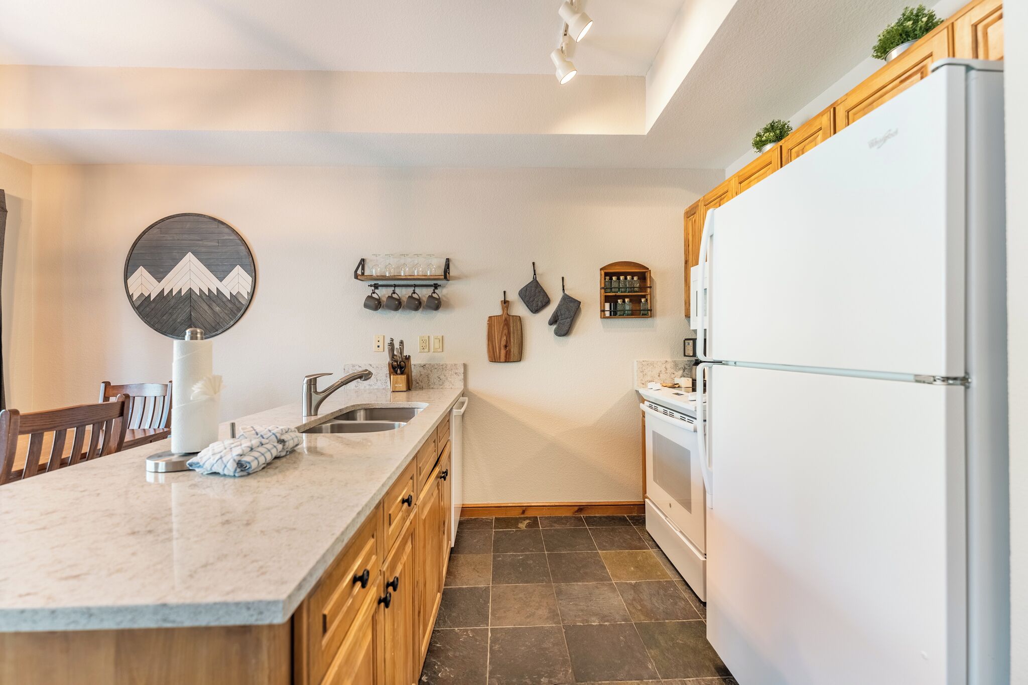 Uma cozinha moderna com bancada de mármore, armários de madeira, geladeira branca e forno embutido.