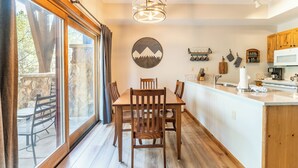Un espace repas avec une table et des chaises en bois, un lustre et une vue dégagée grâce à de grandes fenêtres.