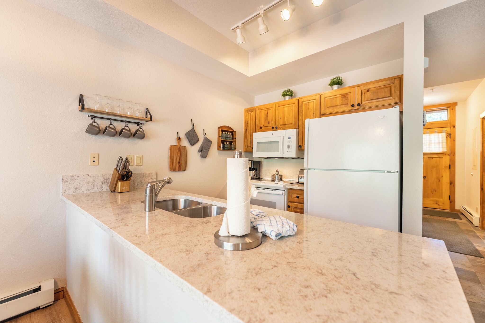 A kitchen with a marble countertop, stainless steel sink, wooden cabinets, a microwave, and a refrigerator.