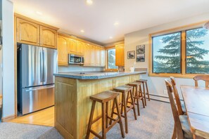 Una cocina con armarios de madera, electrodomésticos de acero inoxidable, una barra con taburetes y una mesa de comedor.